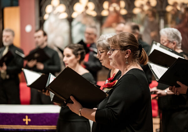 Church Choir during performance at Concert during Christmas Holiday season. Mixed age group of people dressed in all black attire. Interior of Anglican church at night.